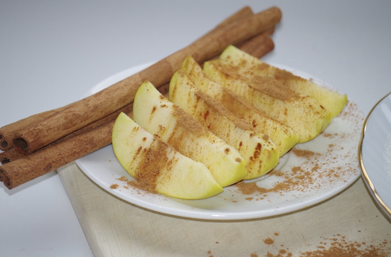 Cinnamon-dusted green apple slices served on a plate with decorative cinnamon sticks.