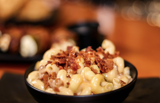 Indulgent macaroni and cheese topped with crispy bacon in a gourmet presentation.