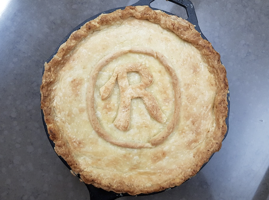 Homemade pie in a cast-iron skillet with a decorative crust and artistic emblem.
