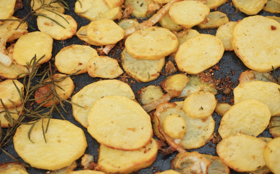 Crispy roasted potatoes with rosemary on a glossy baking tray for delicious home cooking.