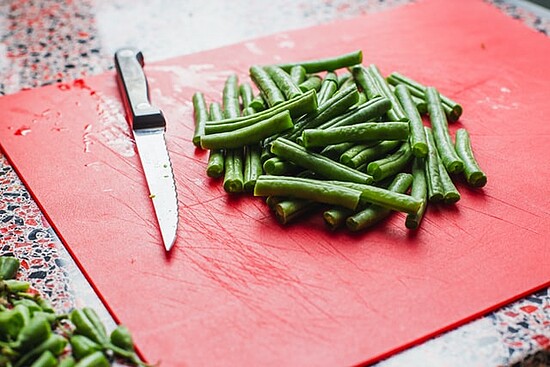 Fresh green beans on a vibrant red cutting board, highlighting kitchen preparation and cooking essentials.