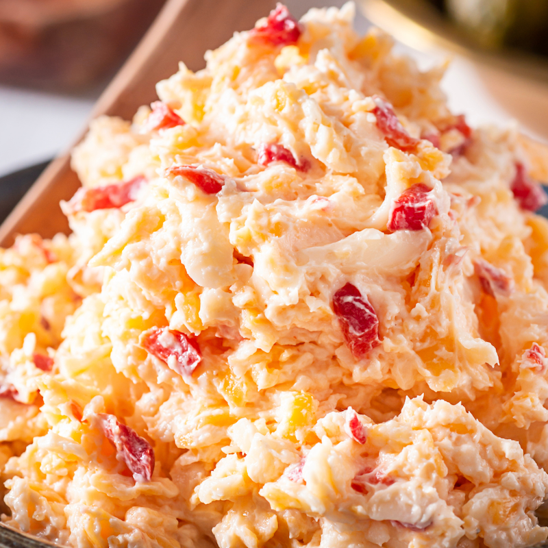 Creamy pimento cheese spread with chopped peppers in a rustic wooden bowl.
